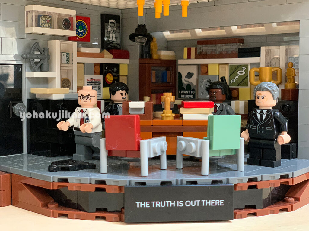 本や書類が積まれたオフィスのレゴ。スーツ姿のミニフィグ4体と、「THE TRUTH IS OUT THERE」の銘板